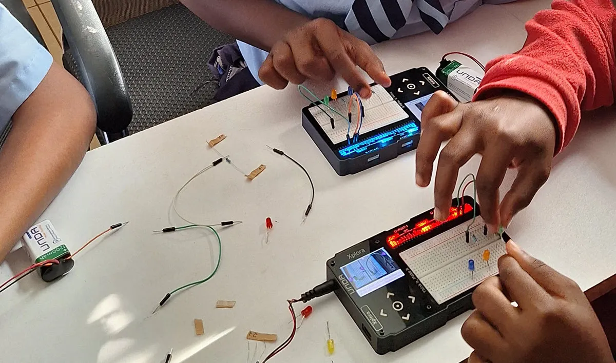 Students wiring LED circuits on two UNDA.Xplora kits, with jumper wires, LEDs and a battery on the table